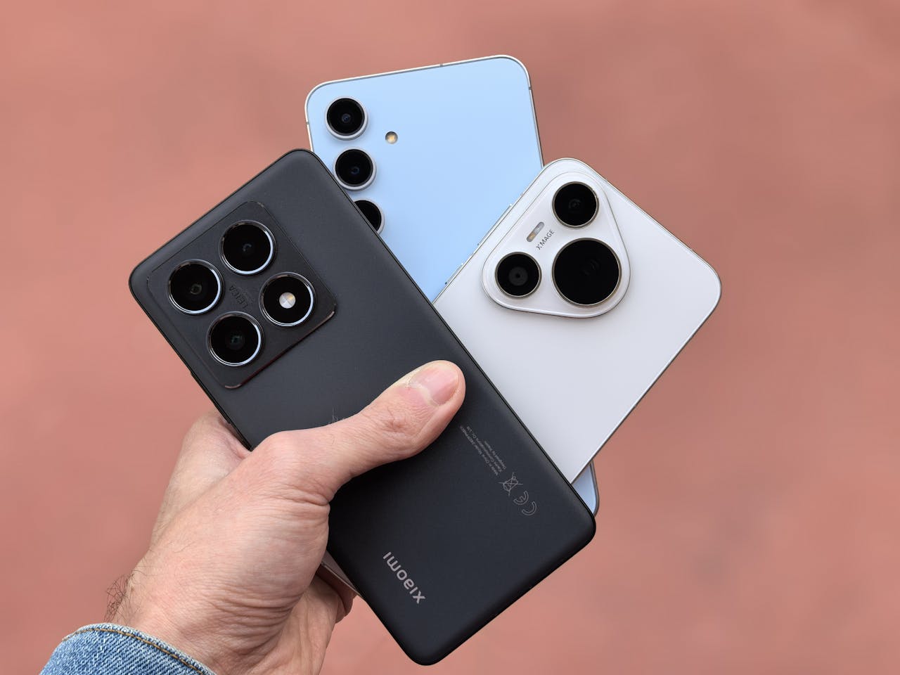 Close-up of a hand holding three modern smartphones with cameras in view, showcasing contemporary design.